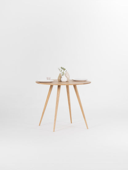 Round dining table with four solid oak legs and natural wood finish