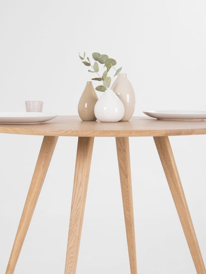 Round dining table with four solid oak legs and natural wood finish