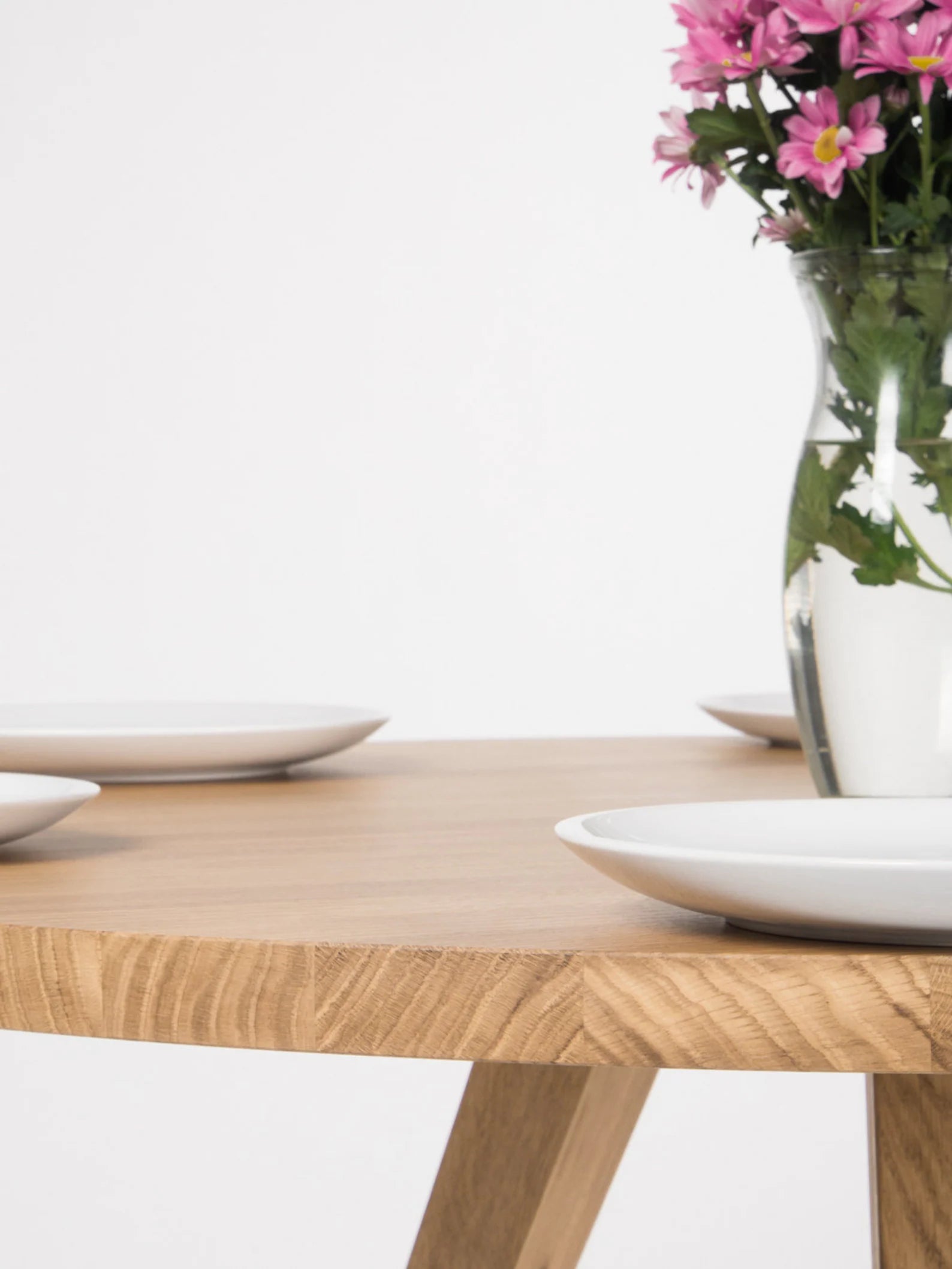 Round dining table made entirely from solid oak, featuring a sculptural 3-leg base and natural finish #material_solid-oak